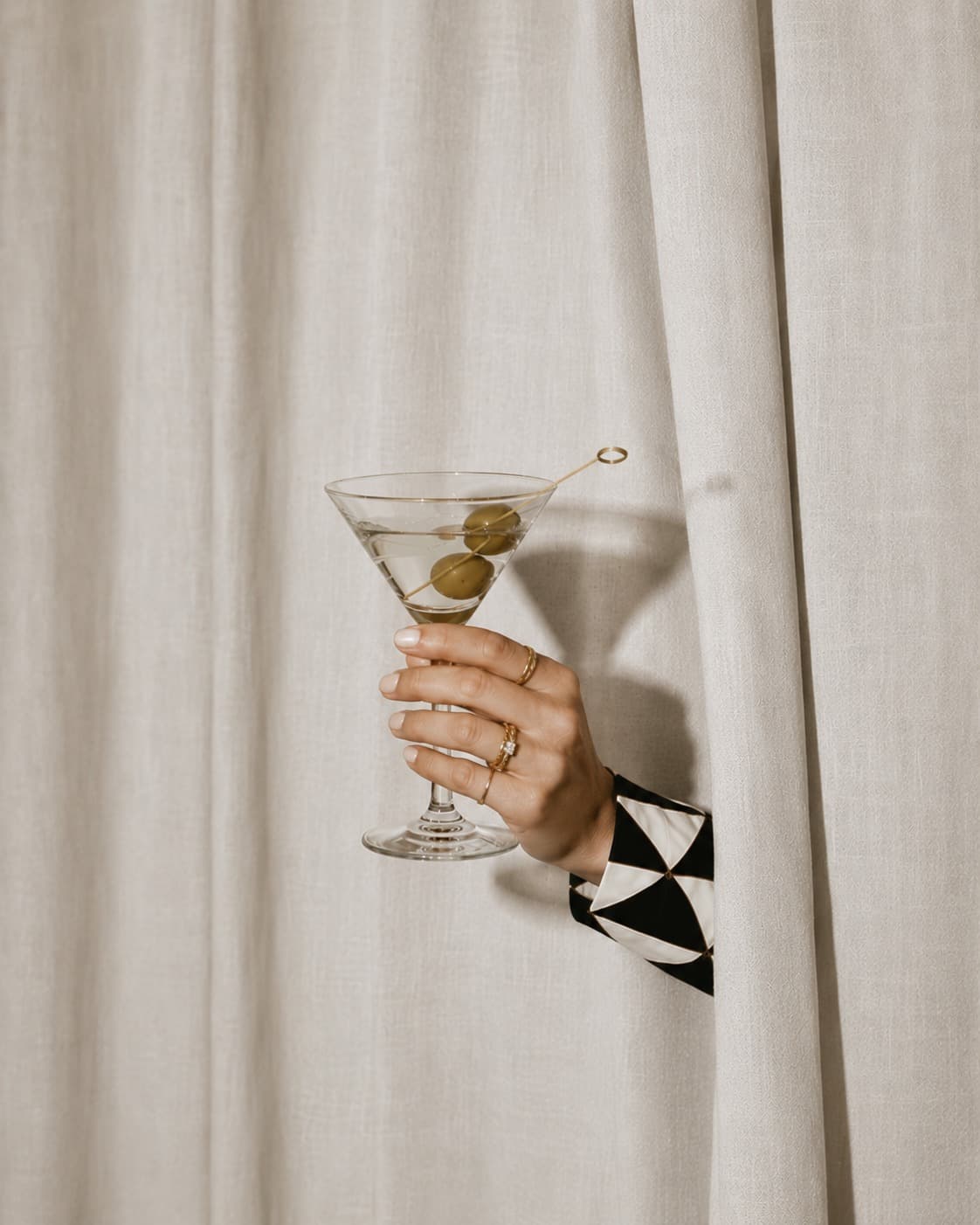 A hand in a graphic sleeve holding a martini through a curtain