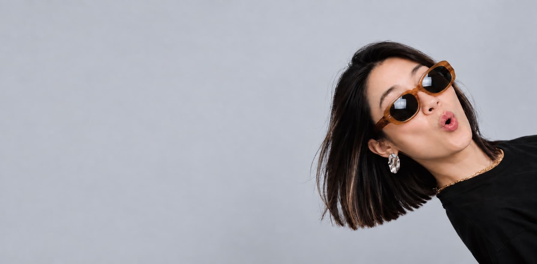 Widelia in tortoiseshell sunglasses, leaning into frame against a grey studio wall